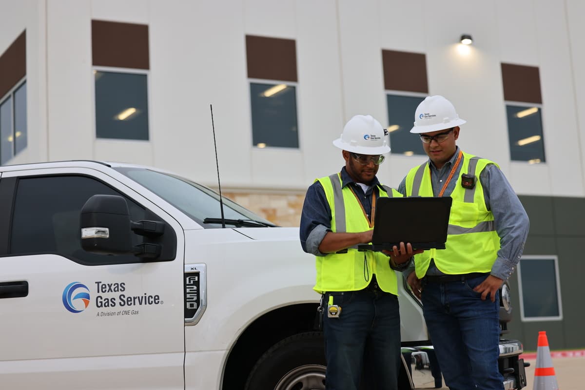 Texas Gas Service employees looking at rugged laptop in front of pickup and building